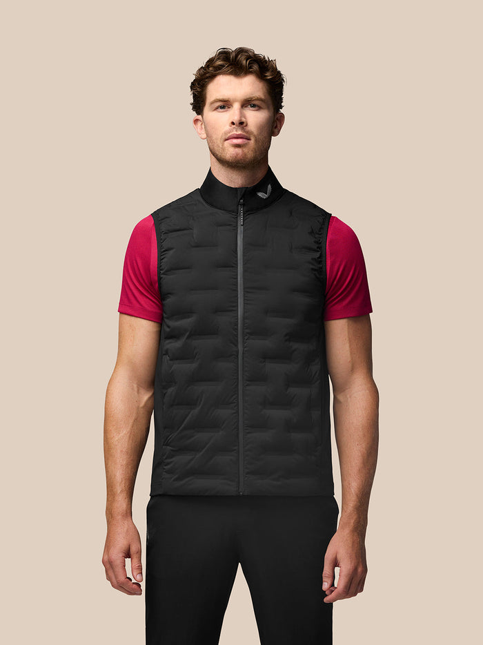 Front view of a man wearing a black Golf Pinnacle Gilet over a red short sleeve top against a beige backdrop.