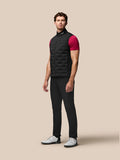 Man wearing black Pinnacle Golf Gilet with stand collar over a magenta tee; sleeveless quilted vest with front zip and Castore branding at the collar and upper back.