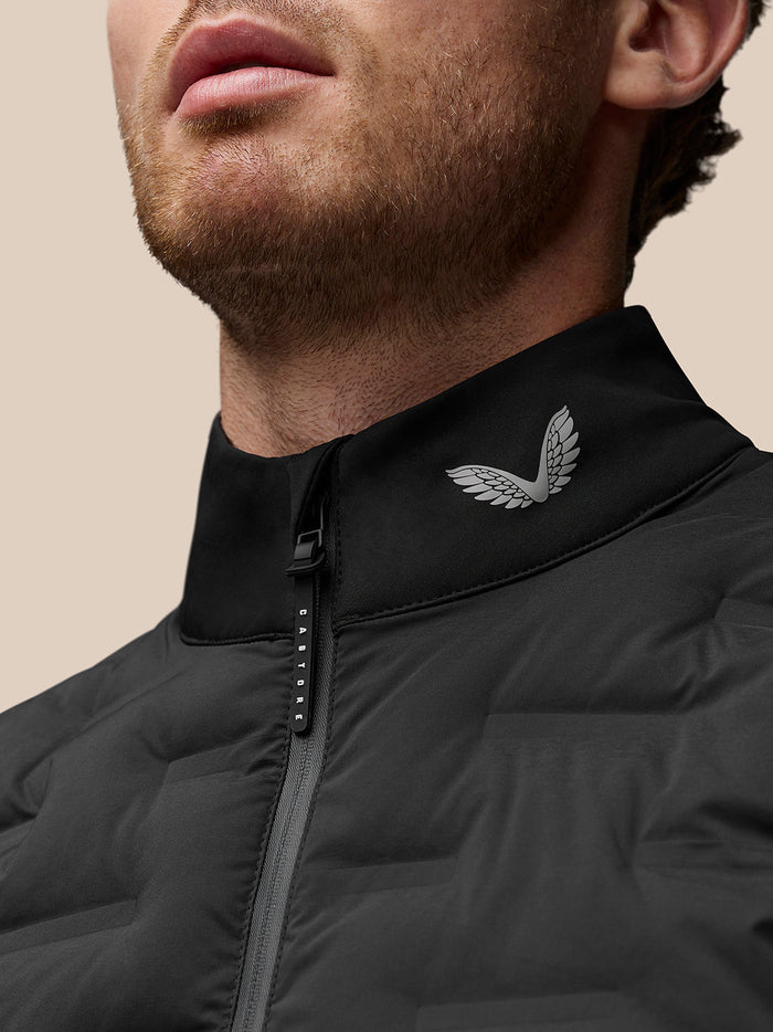Close-up of the stand collar on the black gilet showing a silver wing logo and Protek branded zipper pull.