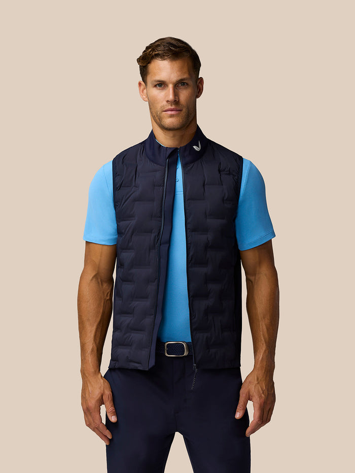 Male model wearing navy quilted Pinnacle Gilet with stand collar and front zip over a light blue polo.