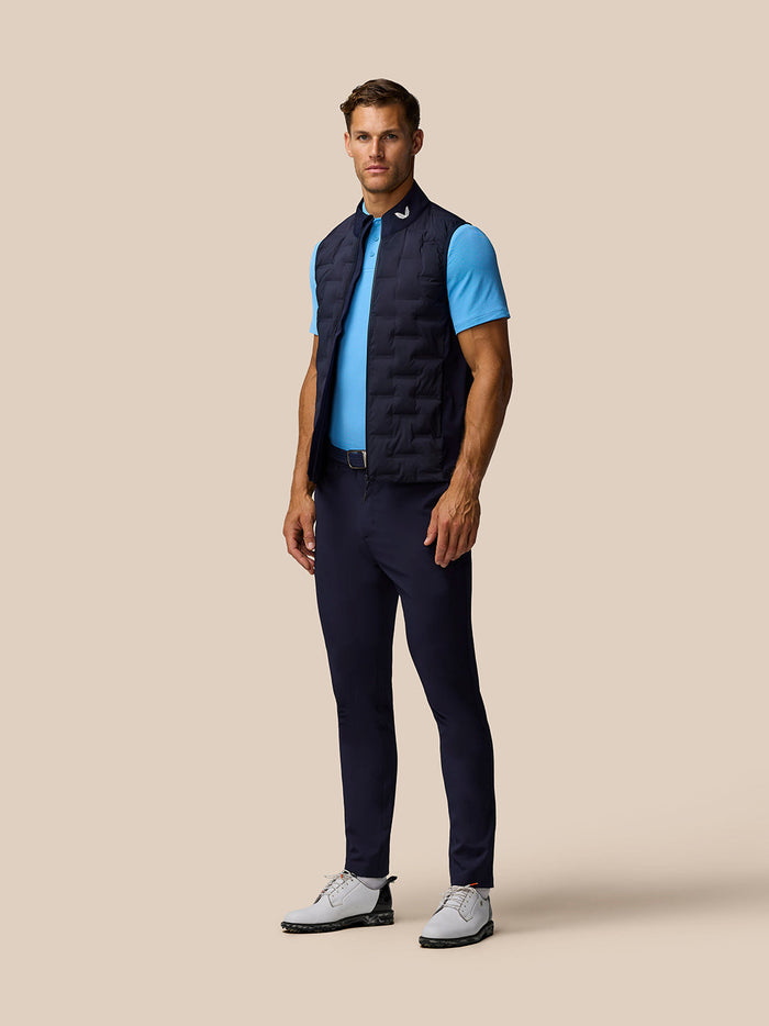 Full length side view of male model in navy Pinnacle Gilet over a light blue polo showing branding at the collar.
