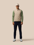 Full body front view of a man in Golf Pinnacle Gilet Mushroom beige vest with green sleeves, cap and navy trousers