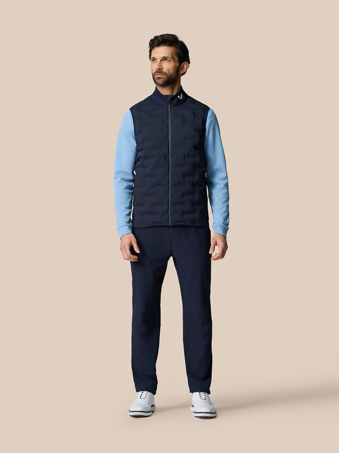 Male model wearing Golf Pinnacle Gilet Midnight Navy with stand collar and sleeveless silhouette over light blue sleeves