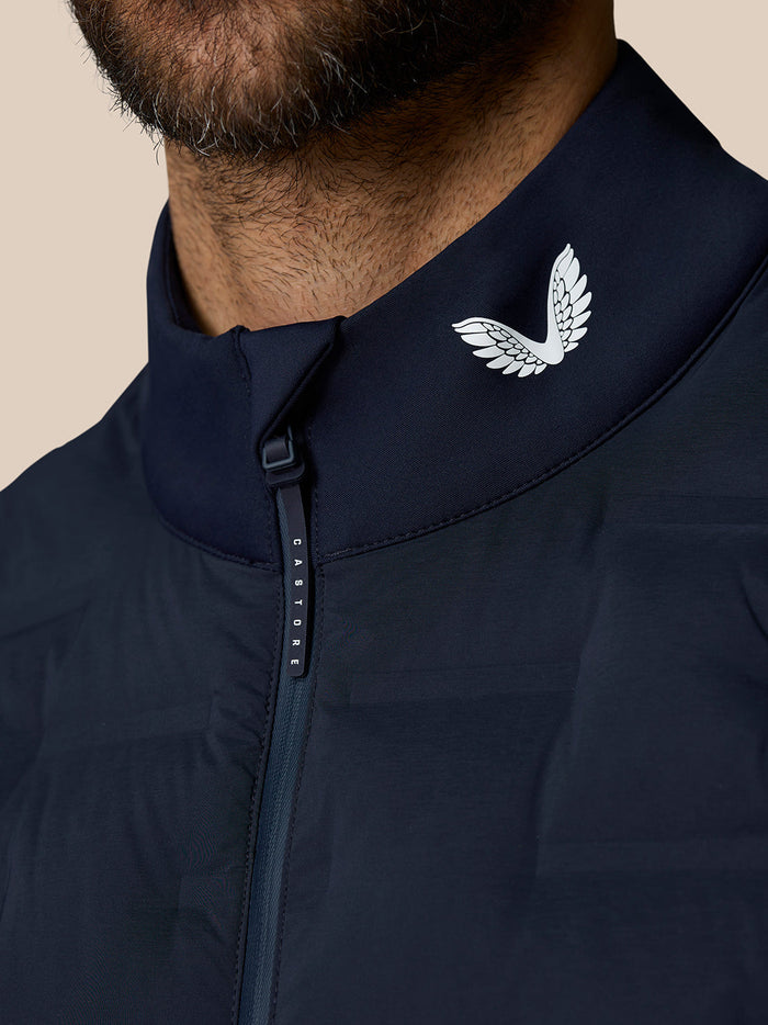 Close-up of navy Pinnacle Gilet collar showing the white Castore wing logo and zipper pull with Castore lettering
