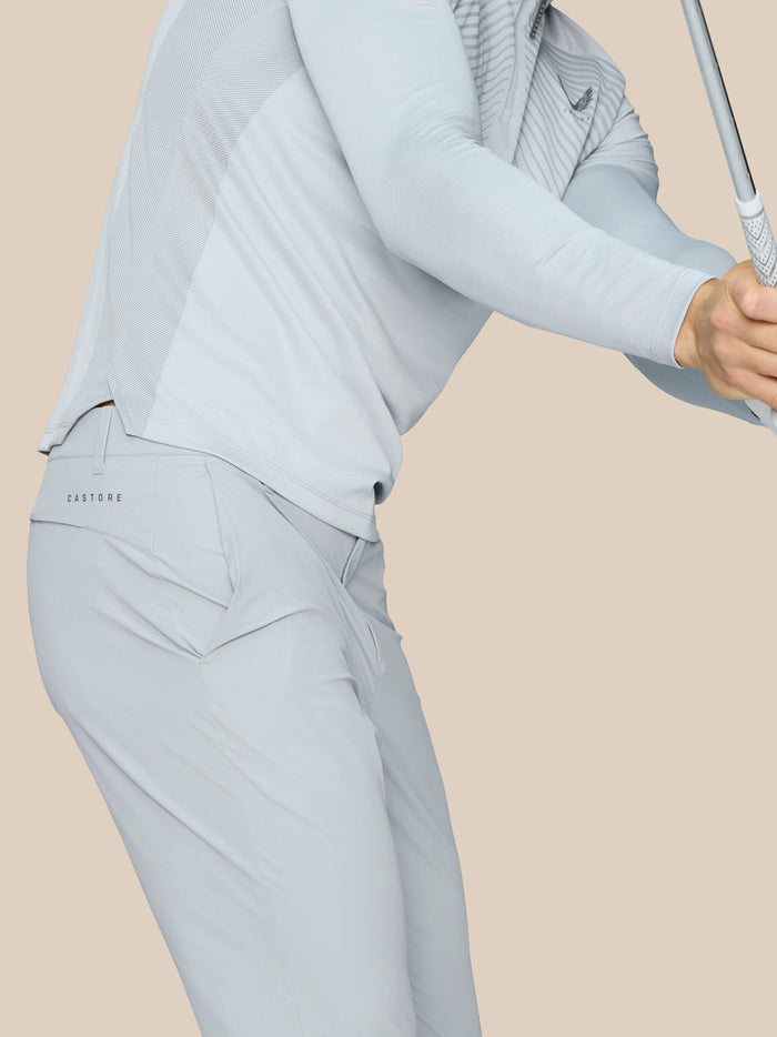 Side view of a golfer wearing light grey Castore Golf Pinnacle trousers, with branding on the right thigh and rear, gripping a golf club.