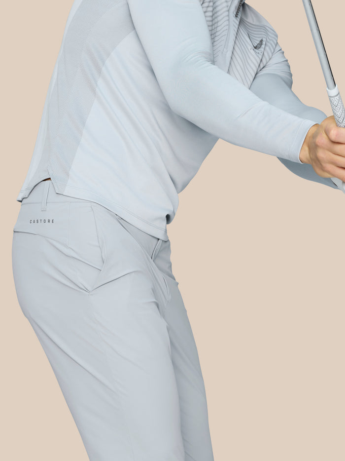 Close-up of light grey Pinnacle trousers showing Castore logo at the hip as hands grip a golf club.