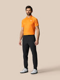 Male model wearing black Golf Pinnacle 32 trousers with an orange polo, Castore branding on the right thigh.