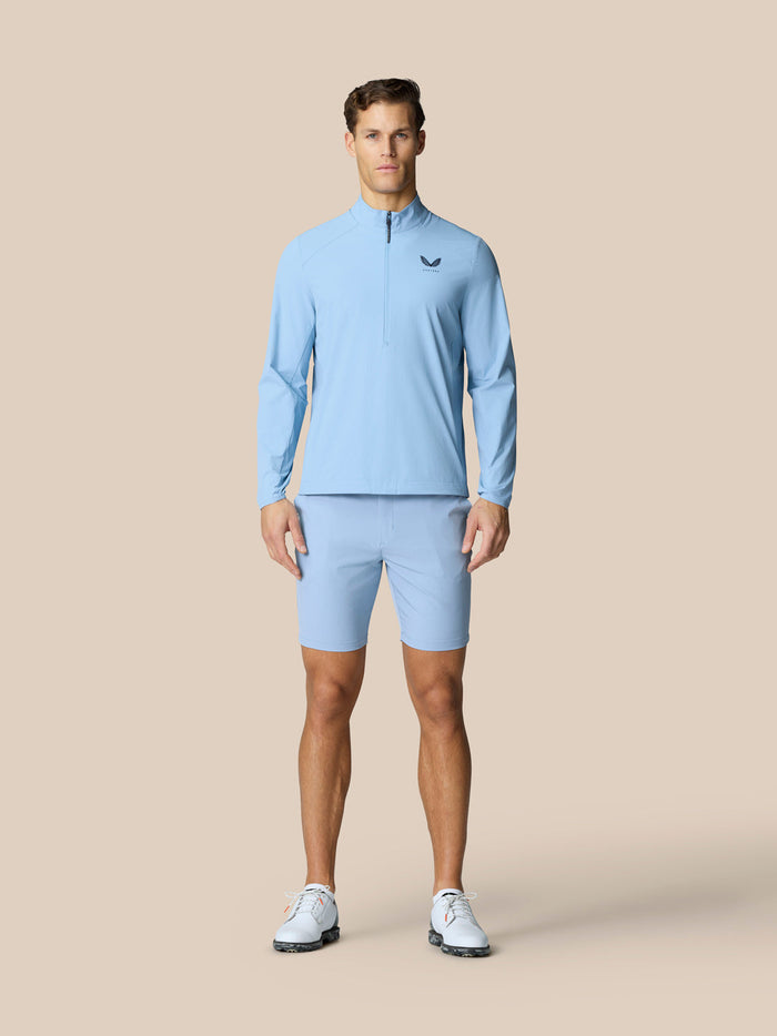 Full-body shot of a male model in sky blue Golf Flex Jacket with matching shorts on a beige background.