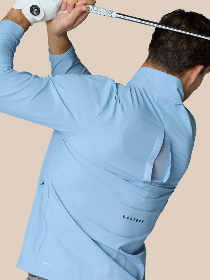 Back view of a man wearing a sky blue Golf Flex Jacket, highlighting the side vent and Castore logo.