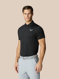 Male model wearing a black Club Graphic Polo with golf ball print and light gray trousers with a gray belt