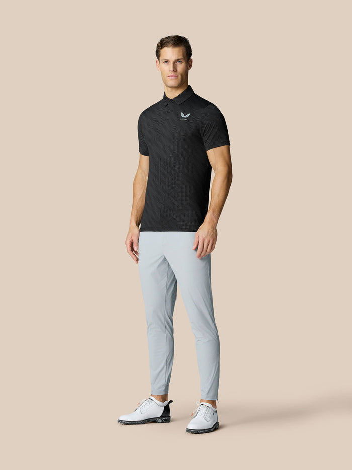 Male model wearing black Club Graphic Polo with golf ball print and light gray pants.
