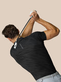 Back view of male model in black Club Graphic Polo with dotted texture Castore branding while swinging a golf club