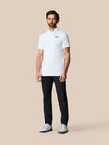 Full-body shot of a man in a white golf ball print Club Graphic Polo with left chest logo and black trousers.