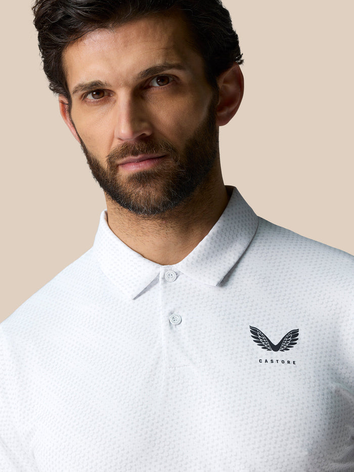 Male model wearing a white textured polo with Castore logo on the chest, beige background.