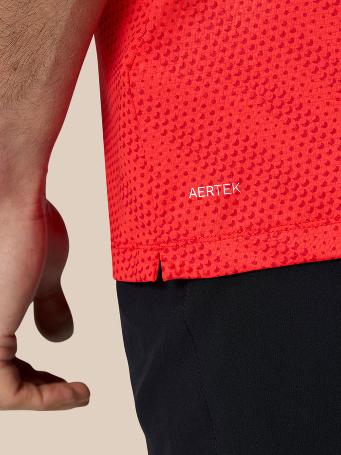 Close up of red polo fabric showing AERTEK branding near the hem