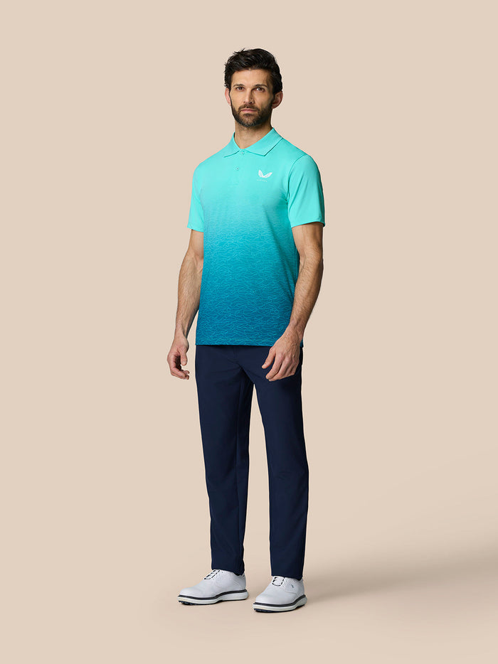 Full-body shot of a man wearing the Club Graphic Polo in a light aqua gradient with navy pants and white golf shoes.