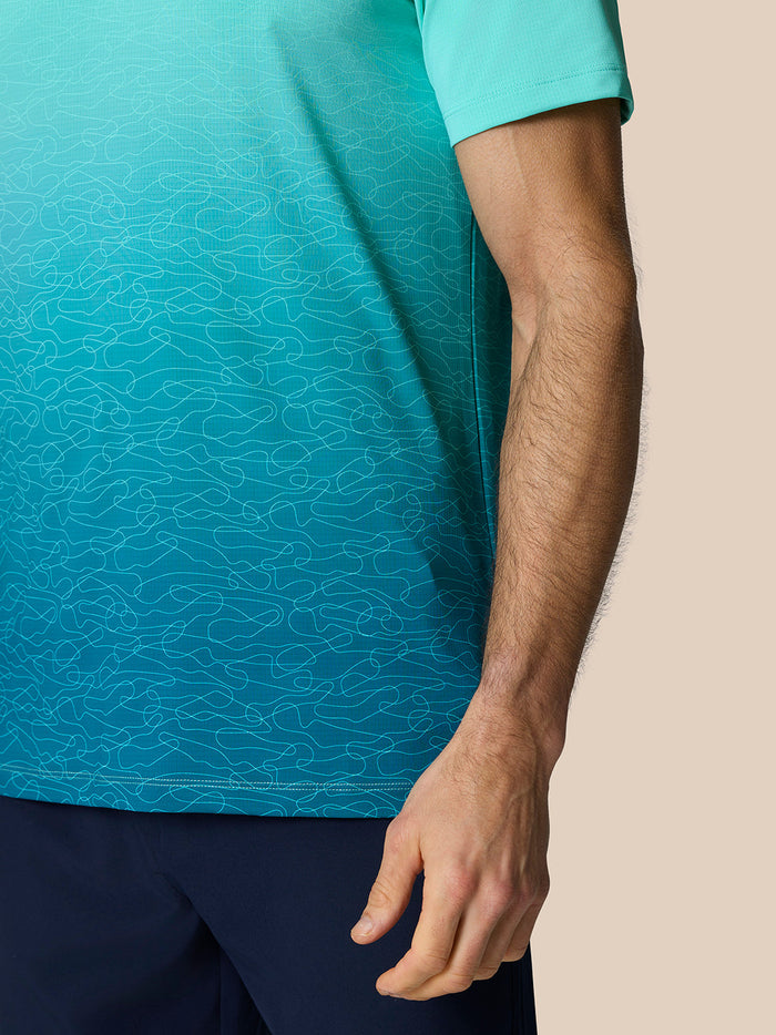 Close-up of a model's arm wearing the Club Graphic Polo with short sleeves and teal to aqua ombre print.