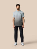 Full front view of a man in a light blue gradient polo with the Castore logo on the left chest, dark trousers and white sneakers.