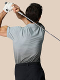 Back view of a man wearing a light grey Castore golf polo with an ombre lower panel and branding along the back, swinging a club.