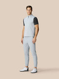 Male model in light grey sleeveless golf gilet layered over a black dotted tee, with light trousers and white golf shoes
