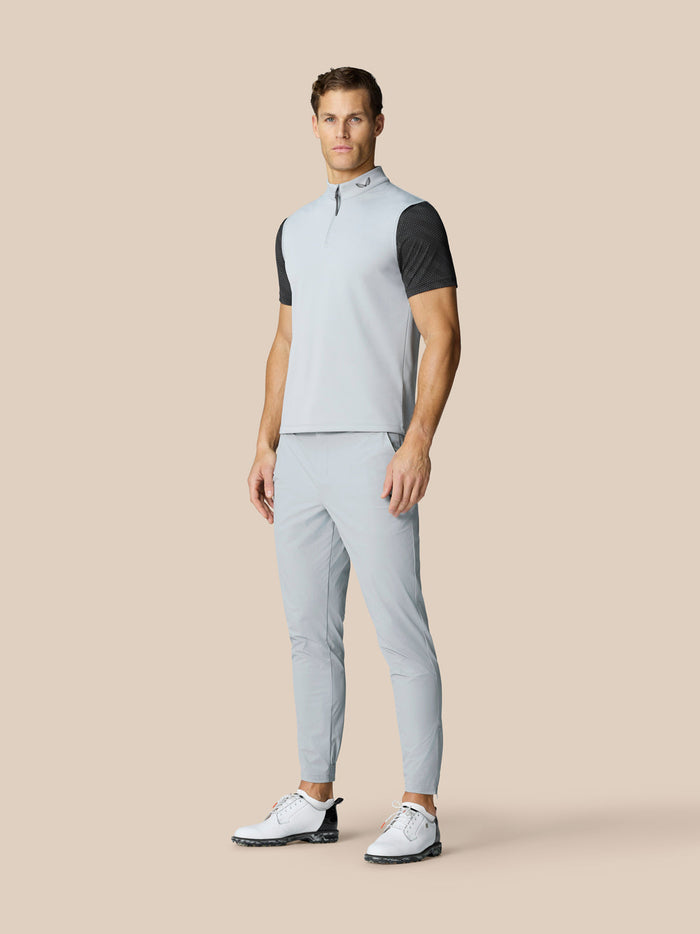 Male model in light grey sleeveless golf gilet layered over a black dotted tee, with light trousers and white golf shoes