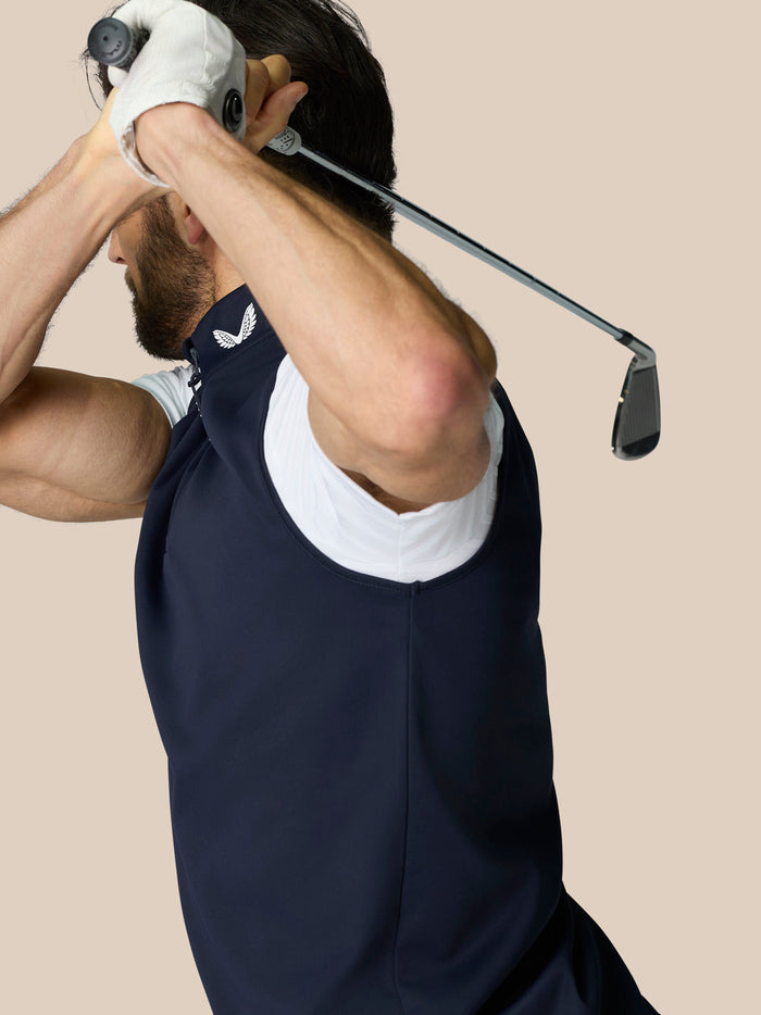 Male athlete wearing navy Club 1/2 Zip Gilet with high neck and white undershirt, lifting a golf club mid swing