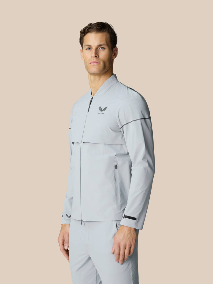 Male model wearing light grey Golf Pinnacle LVS Woven Jacket from the front with zip closure and chest logo