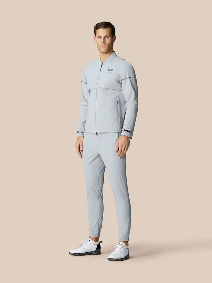 Full length shot of a male model in a matching light grey Golf Pinnacle LVS Woven Jacket and pants with white golf shoes