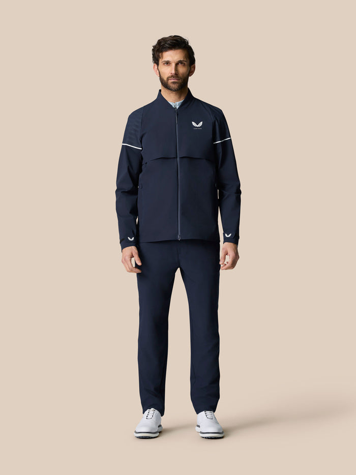 Male model wearing navy Golf Pinnacle LVS Woven Jacket with zip front vented sleeves and white sleeve piping.