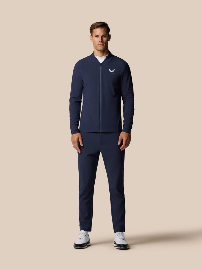 Male model wearing navy winter golf outfit with matching jacket and trousers against a beige background