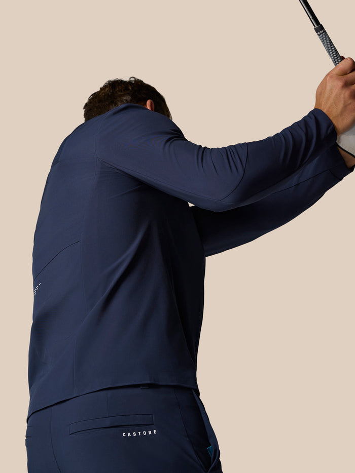 Back view of navy golf winter trousers with Castore branding on rear pocket and raised arm holding a golf club