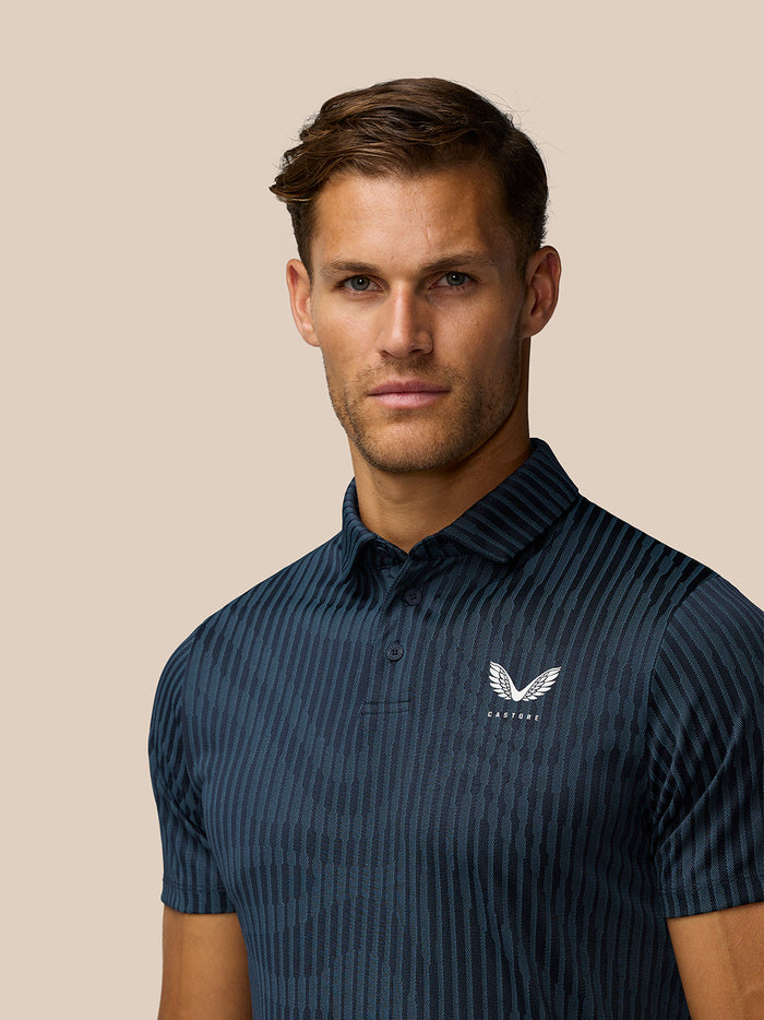Close-up of Castore logo on the left chest of the striped Midnight Navy Golf Pinnacle Glow Polo.