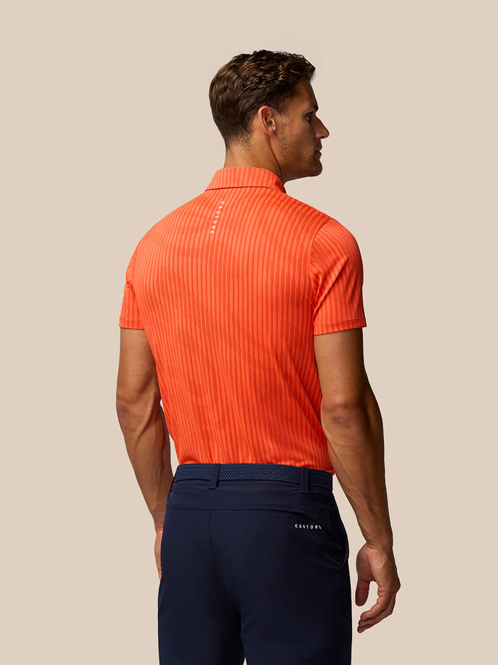 Back view of a man wearing the bright orange Golf Pinnacle Glow Polo with striped knit pattern and Castore branding on the back.