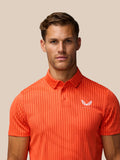 Close-up of bright orange Golf Pinnacle Glow Polo showing the striped knit pattern and Castore logo on the chest.