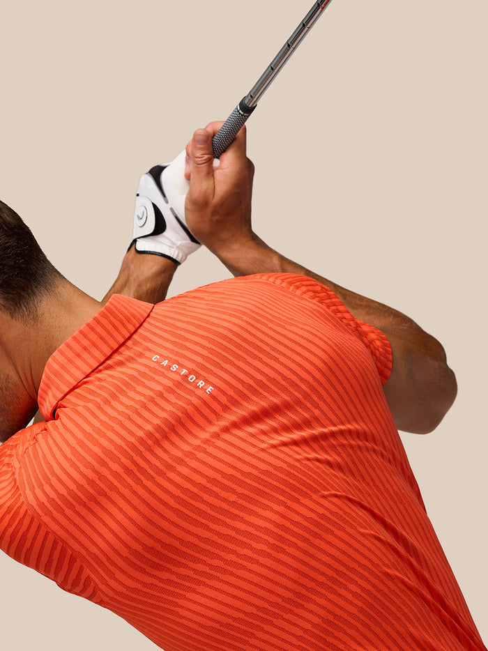 Golfer in Pinnacle Glow Polo bright orange with Castore logo during swing