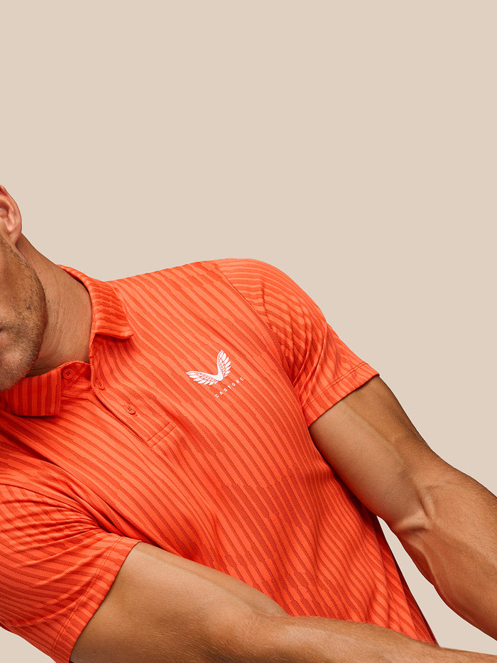 Side-angle view of a man in bright orange striped Golf Pinnacle Glow Polo with Castore logo.