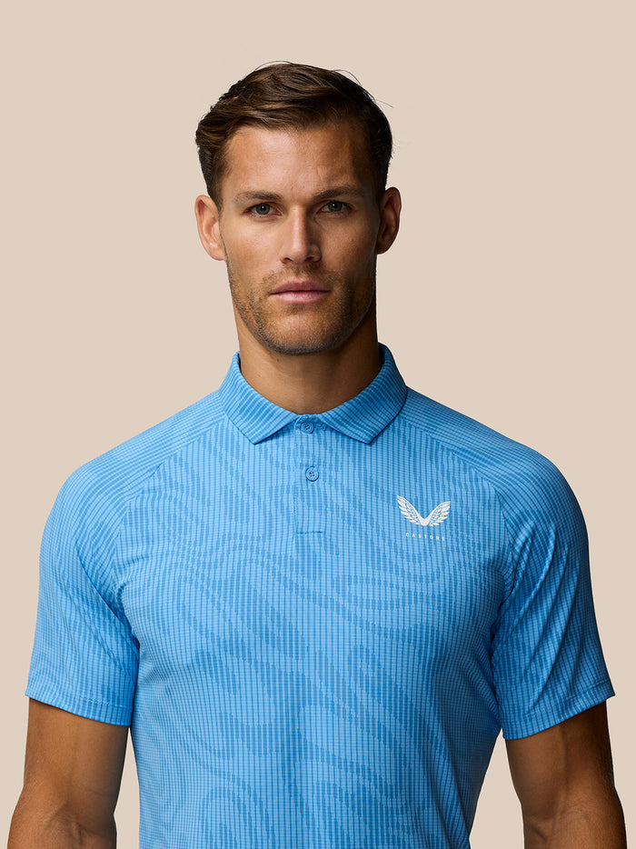 Male model wearing light blue Golf Club Glow Printed Polo with subtle vertical pattern and Castore logo on left chest.