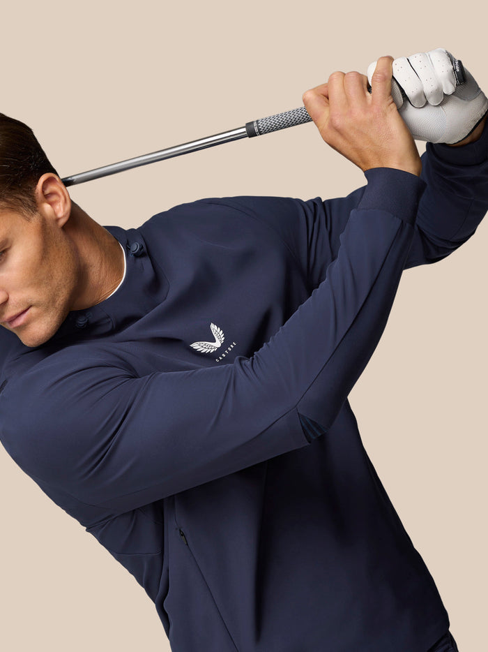 Athletic pose of a man in the midnight navy Golf Pinnacle Performance Hoodie mid swing, holding a golf club with logo on chest.