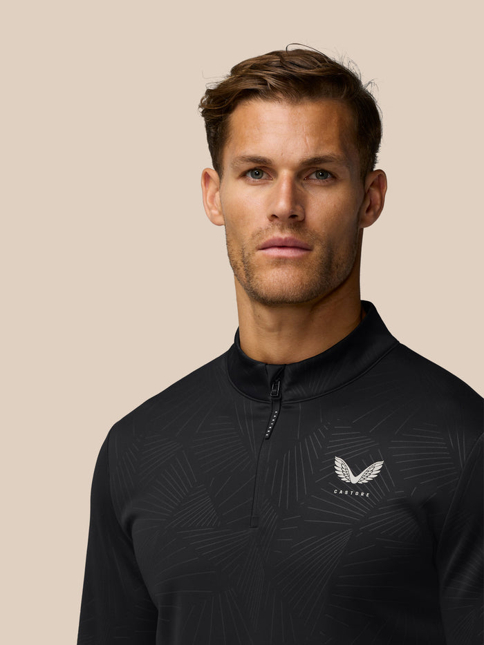 Front view of a man in a black Castore golf top with a winged logo on the chest and a center zipper
