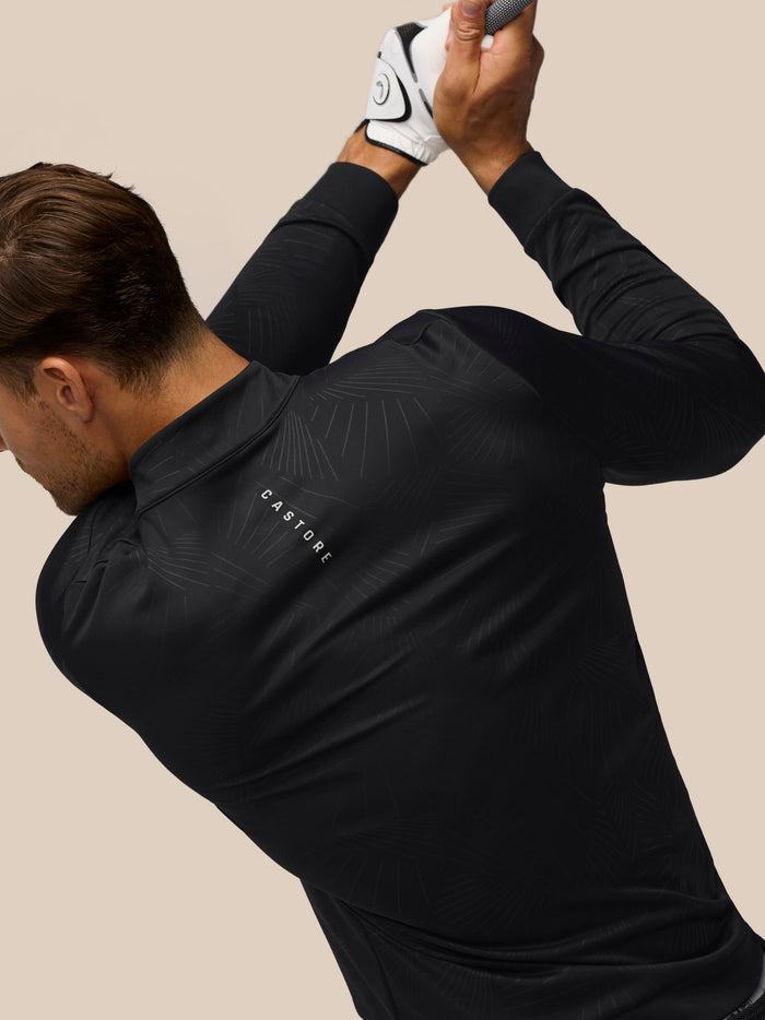Close up of a golfer wearing a black Castore top with a vertical zipper gripping a golf club with a white glove
