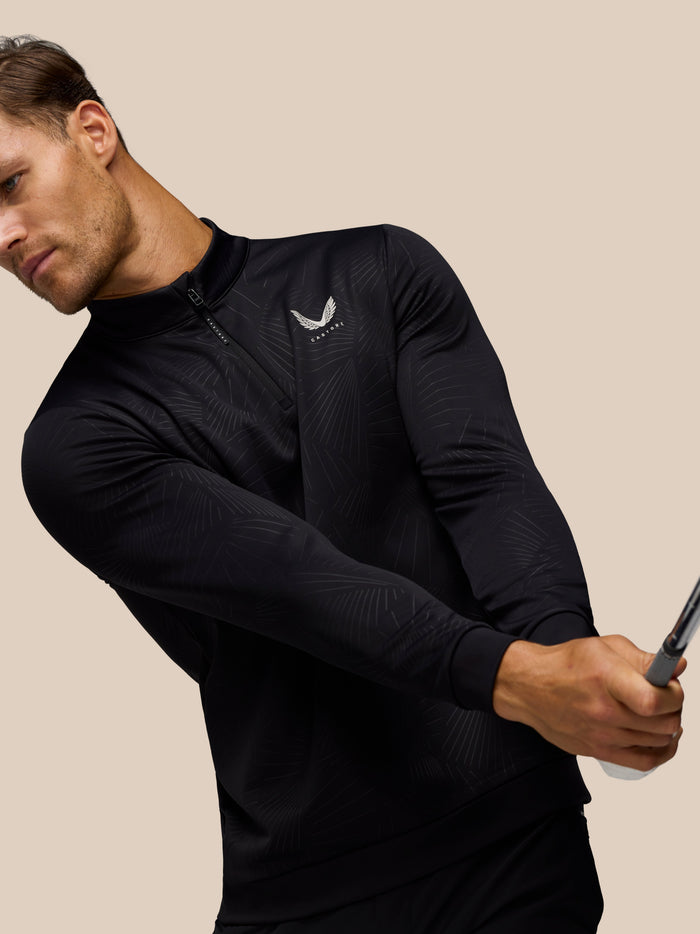 Side view of male model in black golf top with subtle print and Castore logo on chest