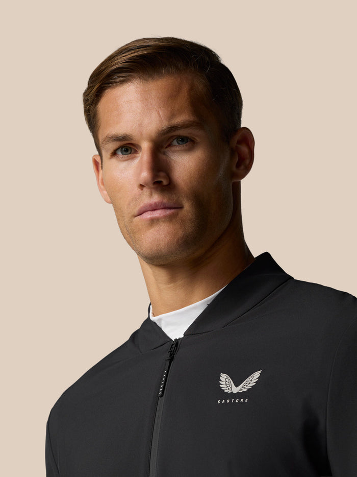 Male model wearing Castore Golf Pinnacle LVS Winter Jacket in black with front zip and left chest logo.