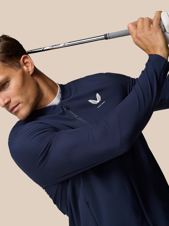 Male golfer wearing a midnight navy LVS Winter Jacket mid swing with a golf club.