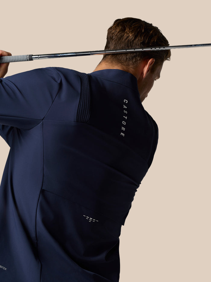 Back view of navy Castore jacket with branding along the back and model standing in a neutral pose
