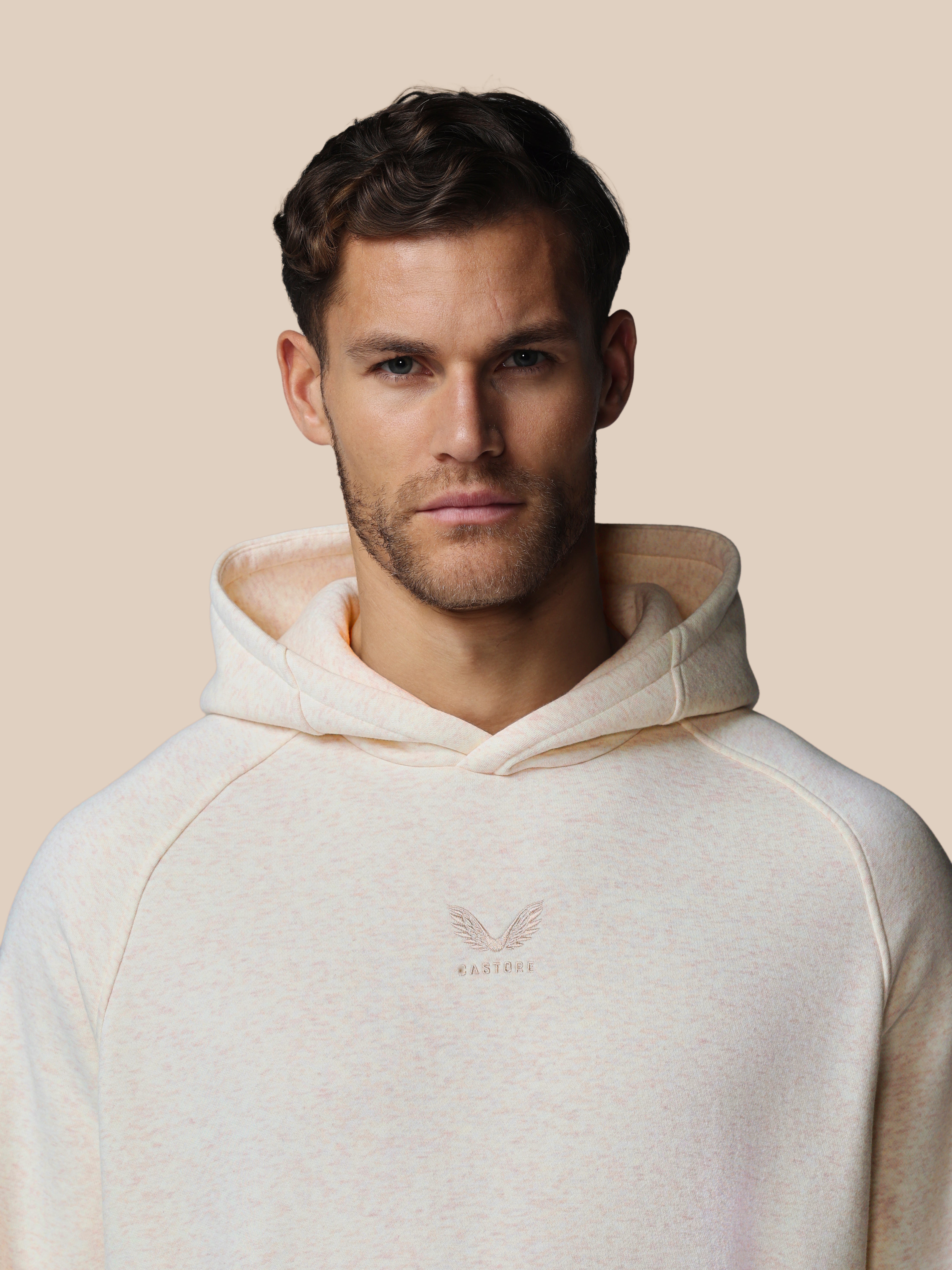 Man wearing a beige hoodie with a logo on a beige background