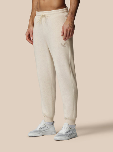 Person wearing beige sweatpants and white sneakers on a beige background