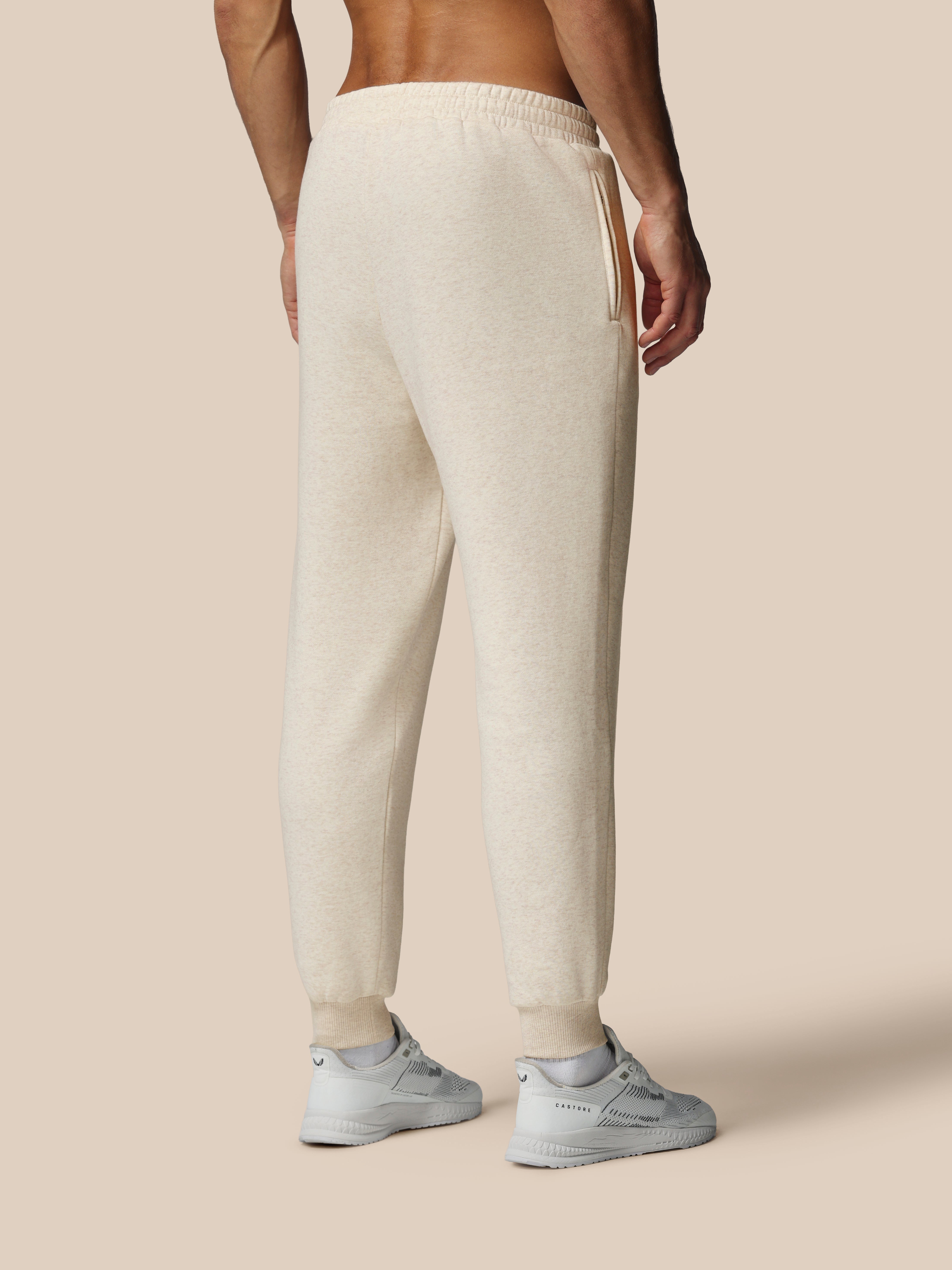 Person wearing beige sweatpants and white sneakers on a beige background