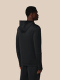 Person wearing a black hoodie and pants on a beige background