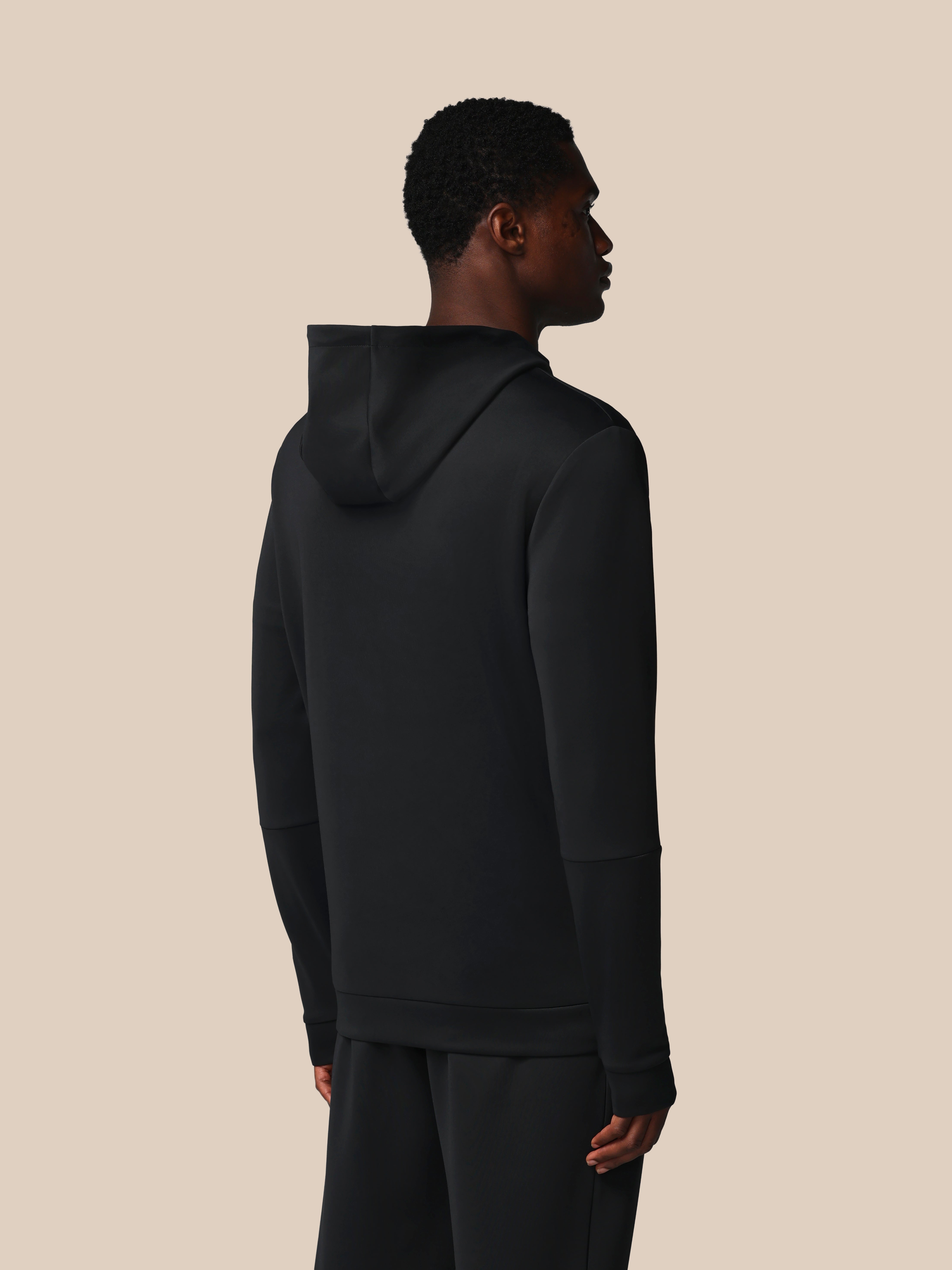 Person wearing a black hoodie and pants on a beige background