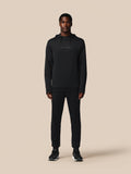 Person wearing a black hoodie and pants on a beige background
